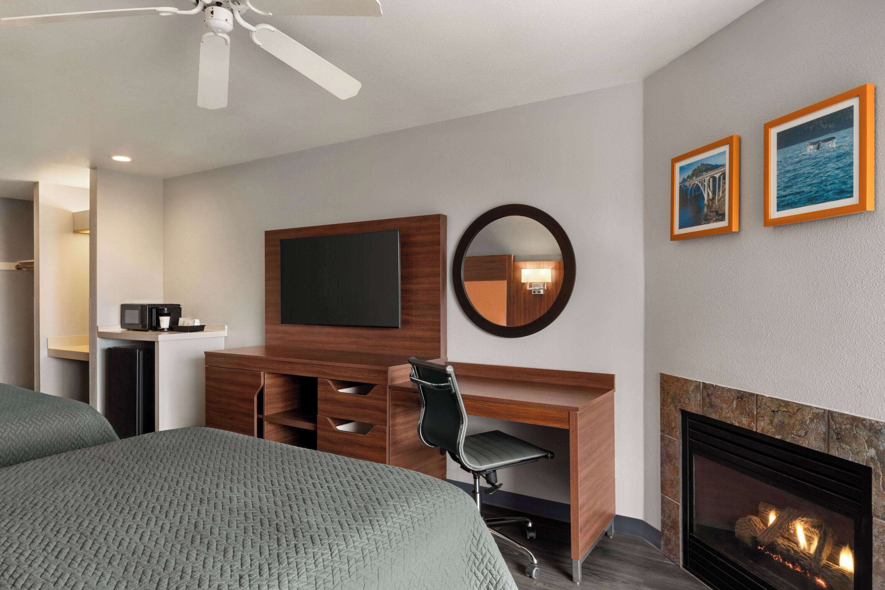 A hotel room with a bed, a desk with a chair, a flat-screen TV, a fireplace, and framed pictures on the wall.