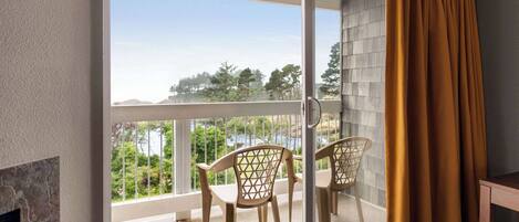 Ein Balkon mit Blick auf Bäume und ein Gewässer, eine Schiebeglastür sowie zwei Korbstühle.