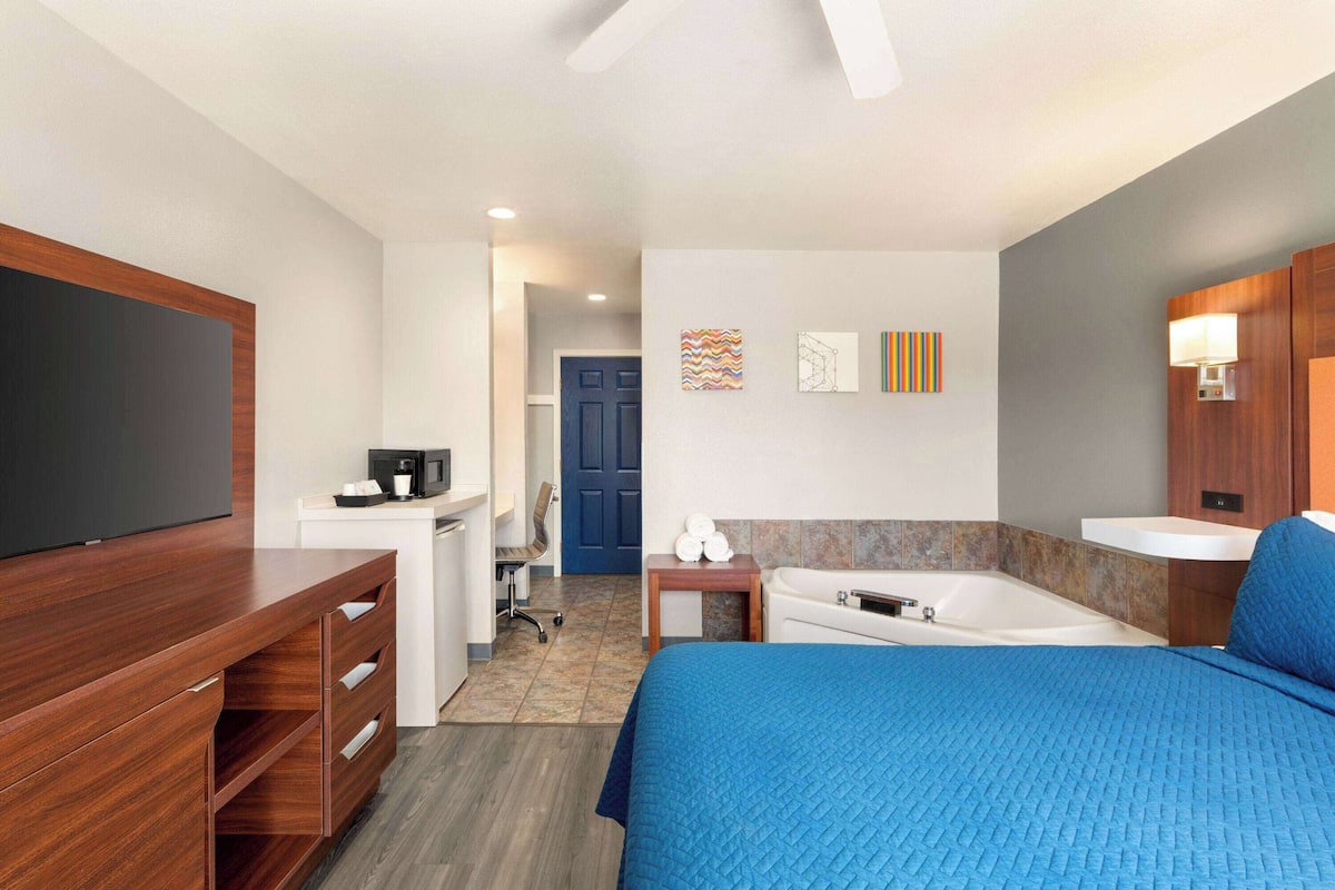 Habitación de hotel con cama, televisión, escritorio con silla, baño con bañera y puerta que da a otra habitación.