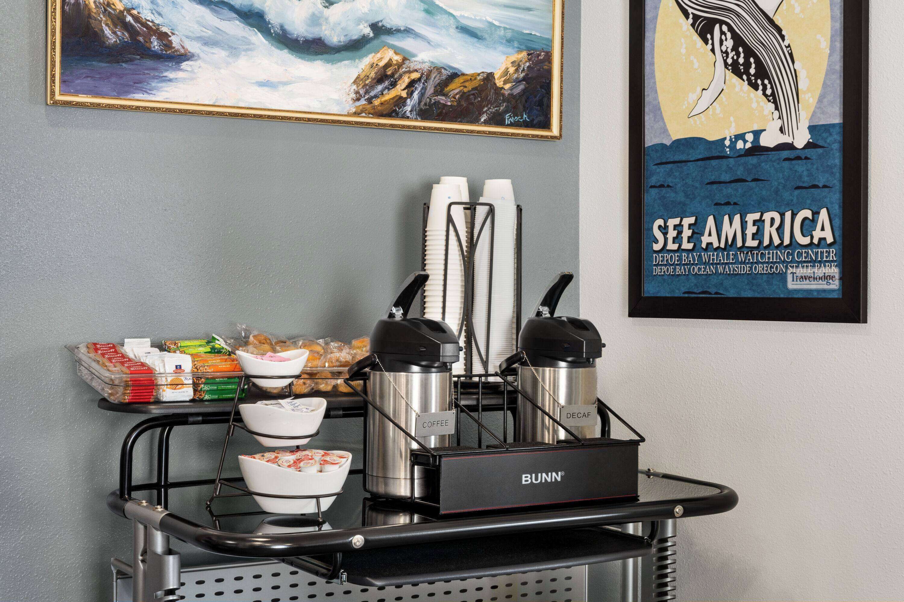 A coffee station with branded dispensers, a framed painting, and a whale watching poster.
