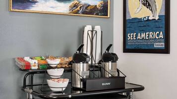 A coffee station with branded dispensers, a framed painting, and a whale watching poster.