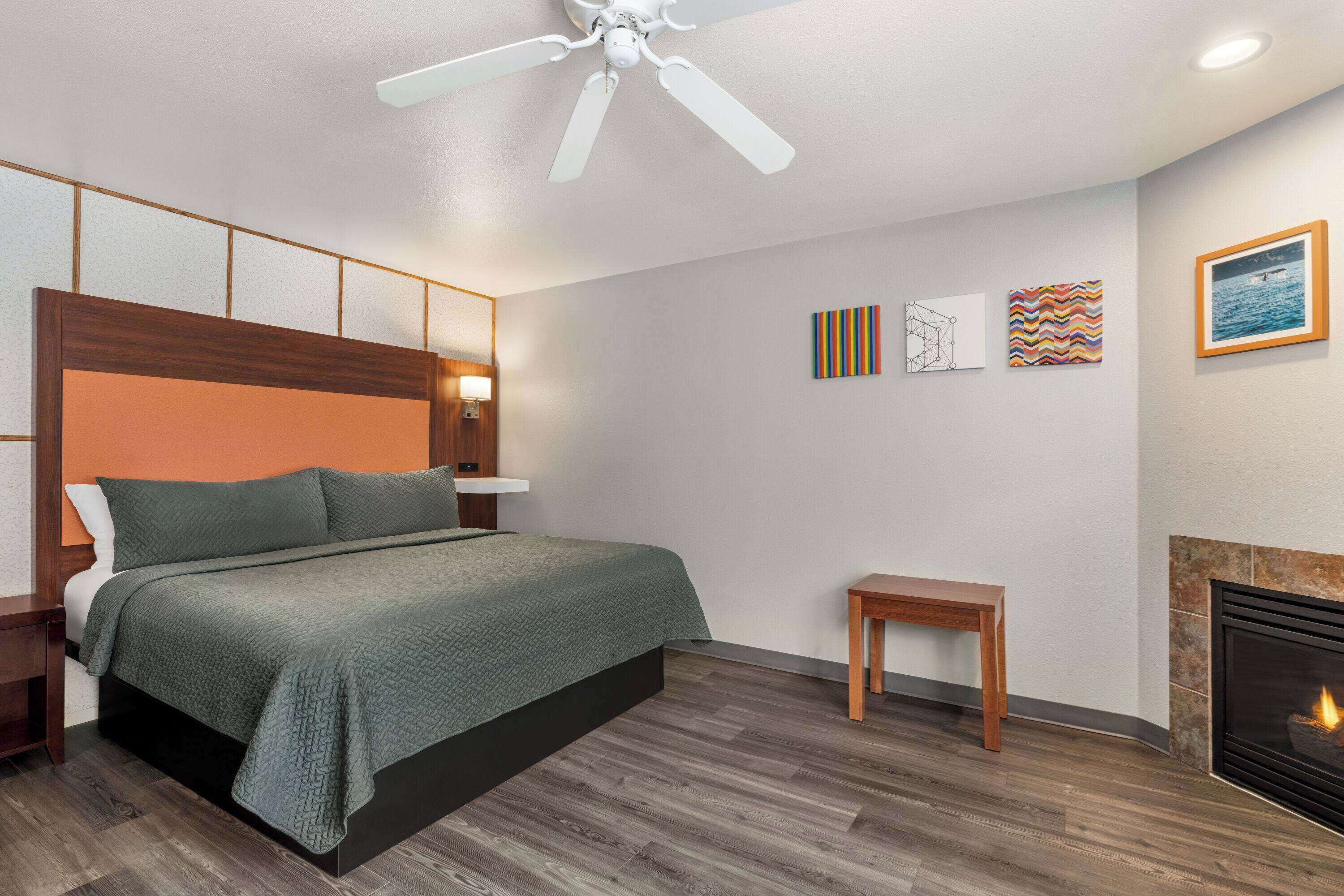Un dormitorio con cama, mesita de noche, banco de madera, chimenea y decoración en la pared.