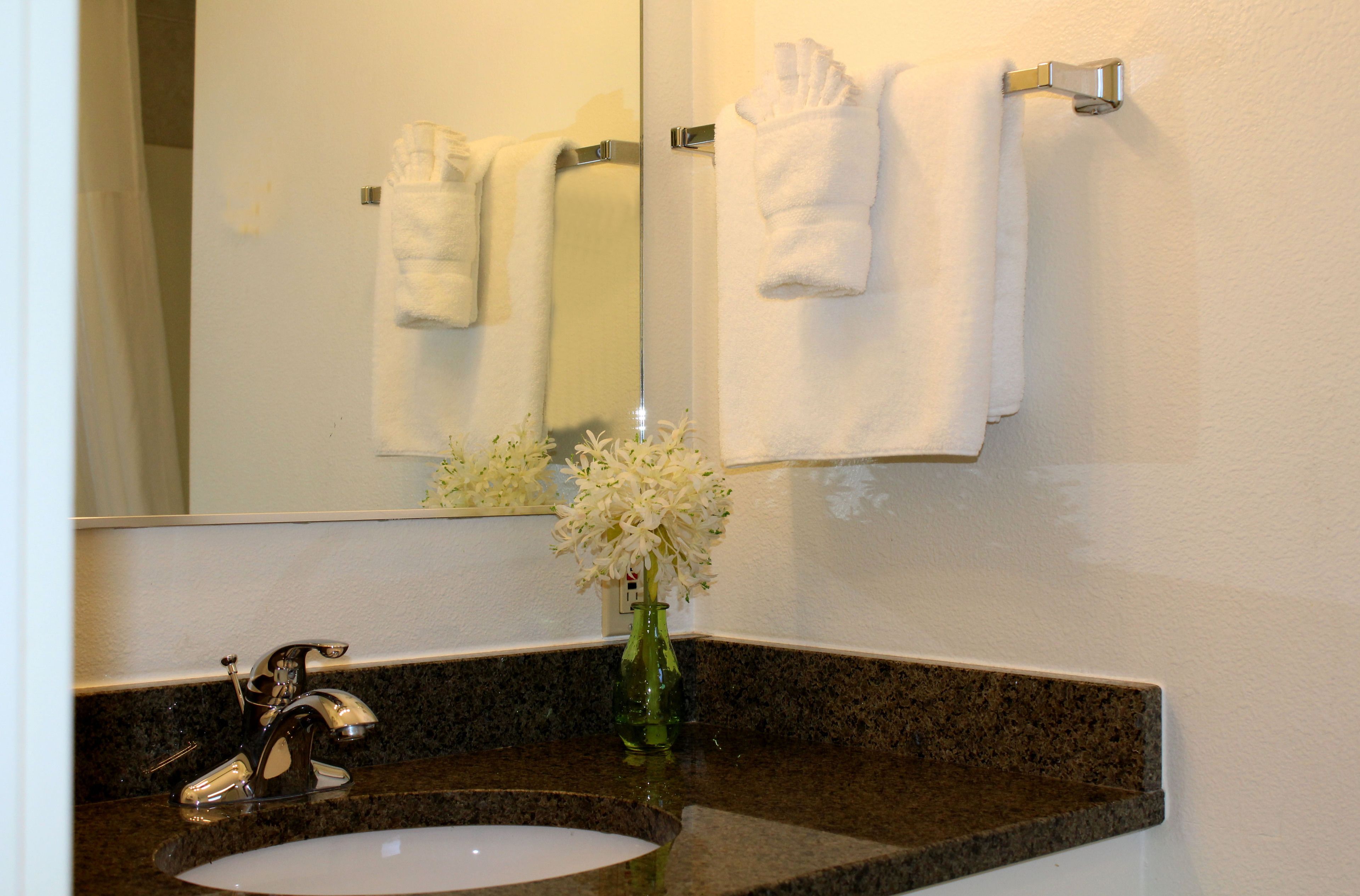 Un baño con lavamanos, espejo, toallero y un florero con flores.