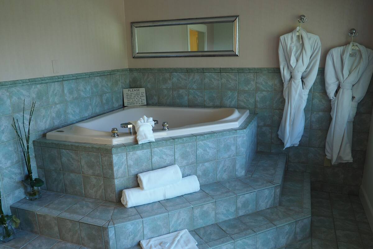 A bathroom with a large bathtub, a mirror above it, and two robes hanging on hooks.