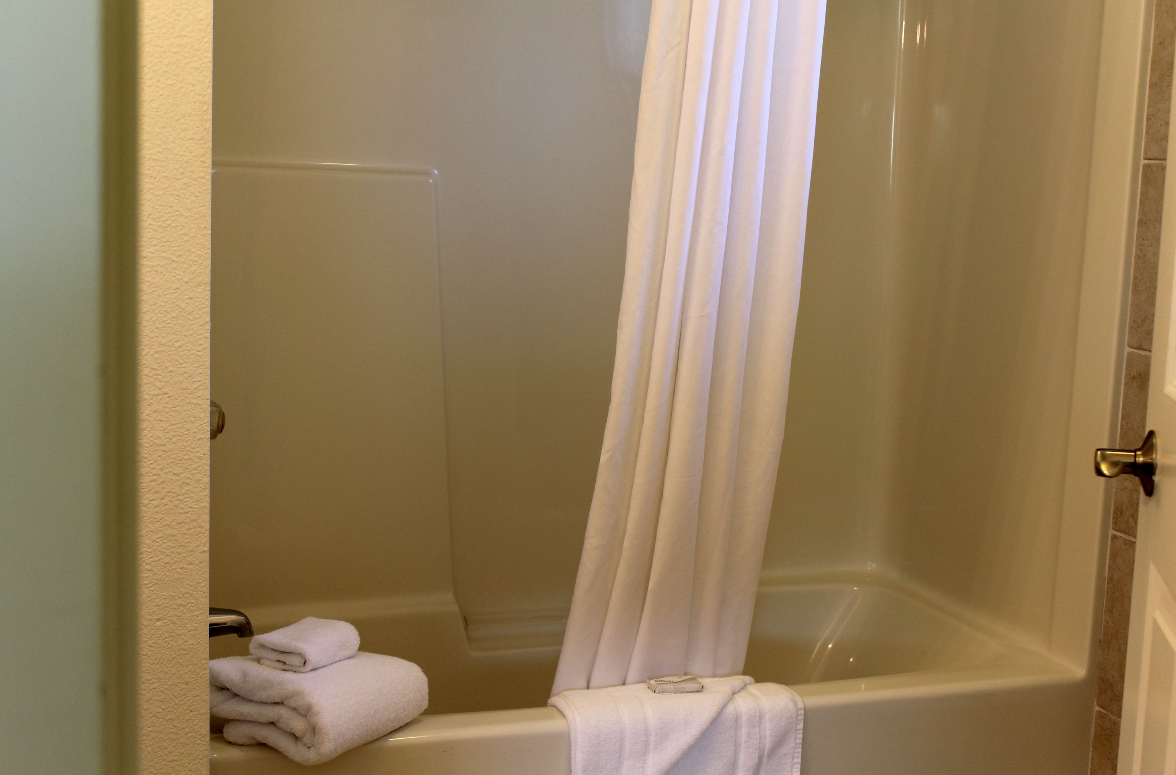A bathroom with a bathtub, a shower curtain, and a stack of towels on the floor.