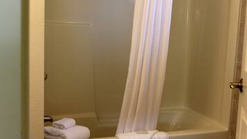 A bathroom with a bathtub, a shower curtain, and a stack of towels on the floor.