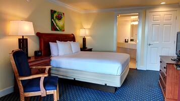 A hotel room with a bed, a desk, a chair, a TV, and a bathroom visible through an open door.