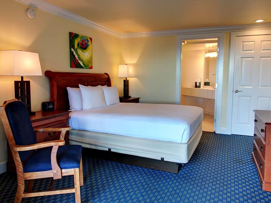 A hotel room with a bed, a desk, a chair, a TV, and a bathroom visible through an open door.