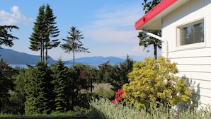 A house with a red roof, surrounded by lush greenery and mountains in the background. - Anacortes Ship Harbor Inn (Anacortes)