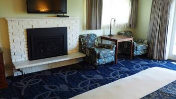 A hotel room with a fireplace, two patterned armchairs, a small table, and a large bed.