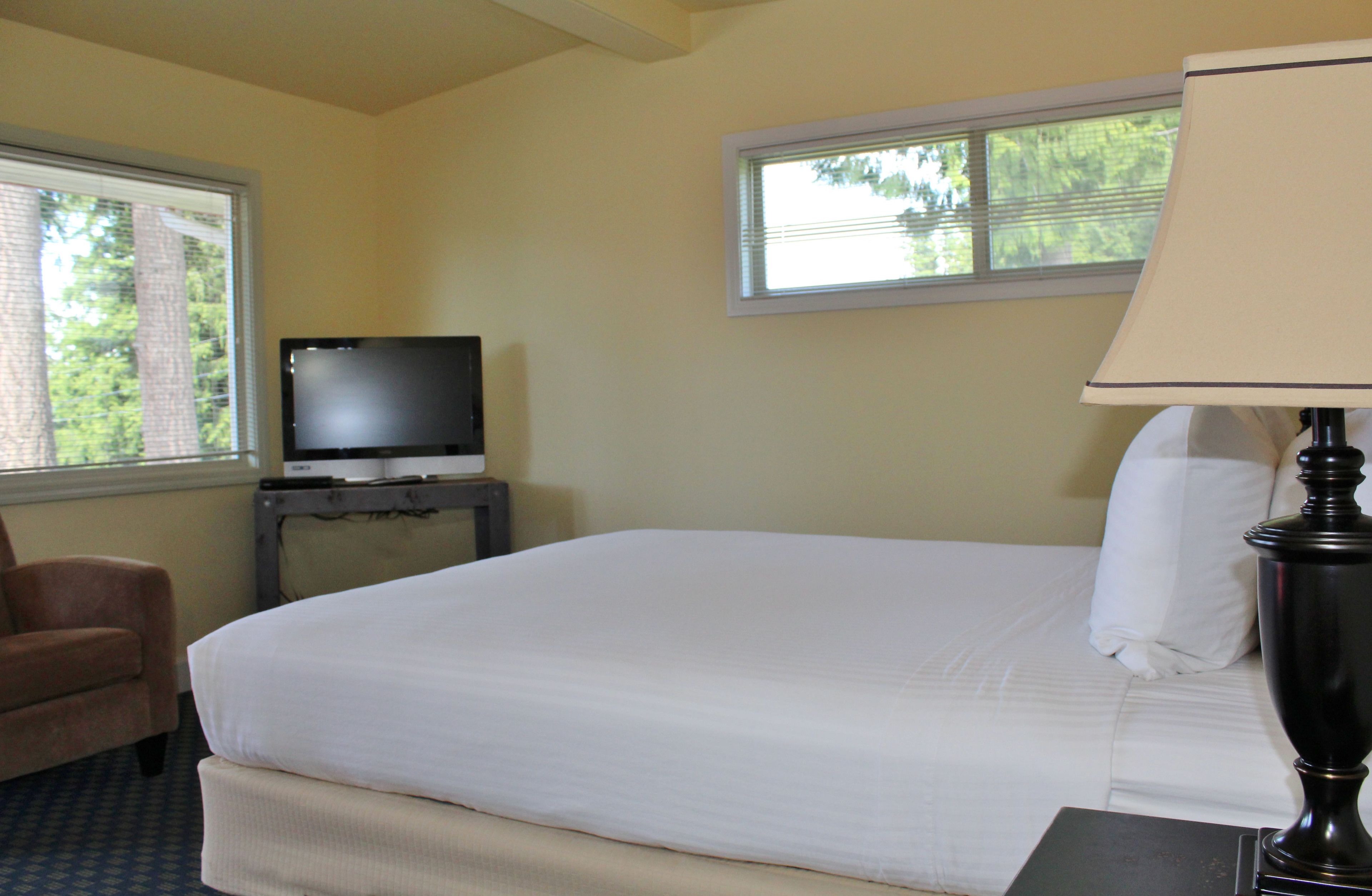 A hotel room with a bed, a television on a small table, a lamp, and a chair.