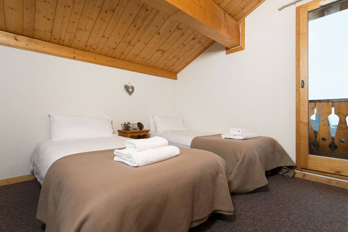 Une chambre d’hôtel avec deux lits, des poutres en bois au plafond, une décoration en forme de cœur et une porte en bois avec un panneau de verre.