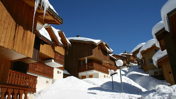 A wooden chalet-style building with balconies, surrounded by snow. - Madame Vacances Les Chalets des Alpages (La Plagne-Tarentaise)