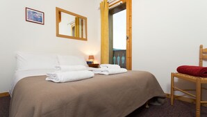 A hotel room with a bed, a chair, a nightstand, a mirror, and a door leading to a balcony. - Madame Vacances Les Chalets des Alpages (La Plagne-Tarentaise)