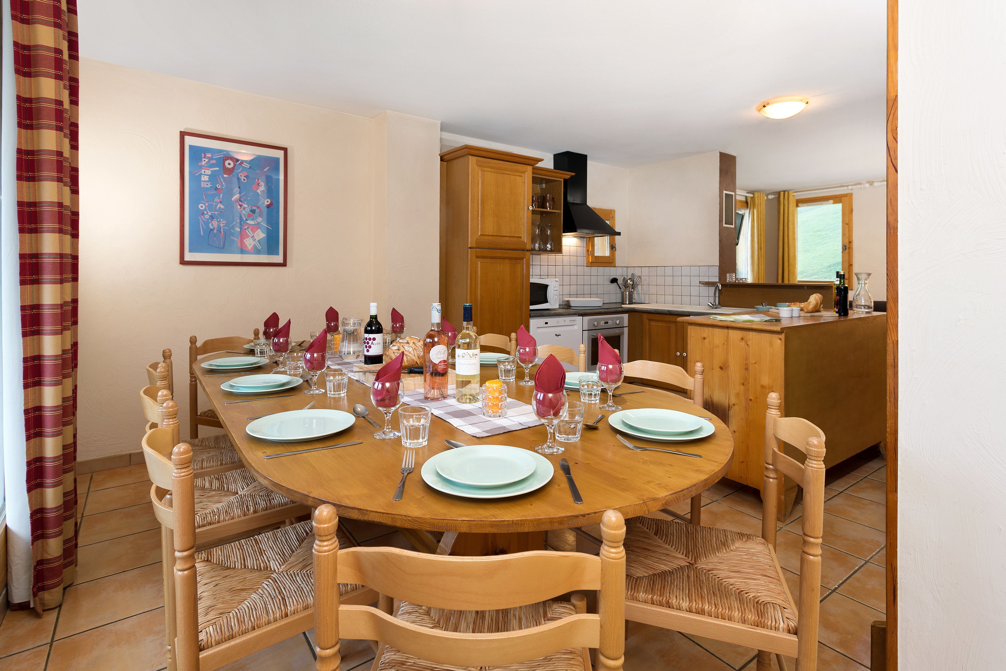 Un coin repas avec une table ronde en bois, dressée pour quatre personnes, entourée de chaises en bois dont les assises sont en osier tressé.