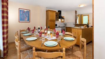 Un coin repas avec une table ronde en bois, dressée pour quatre personnes, entourée de chaises en bois dont les assises sont en osier tressé.