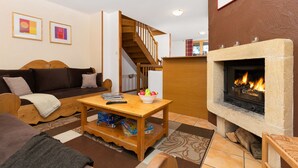 A cozy living room with a fireplace, a sofa, a wooden coffee table, and a staircase leading to an upper level. - Madame Vacances Les Chalets des Alpages (La Plagne-Tarentaise)