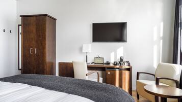 Una habitación de hotel con una cama grande, un escritorio con una silla, un televisor y un armario.