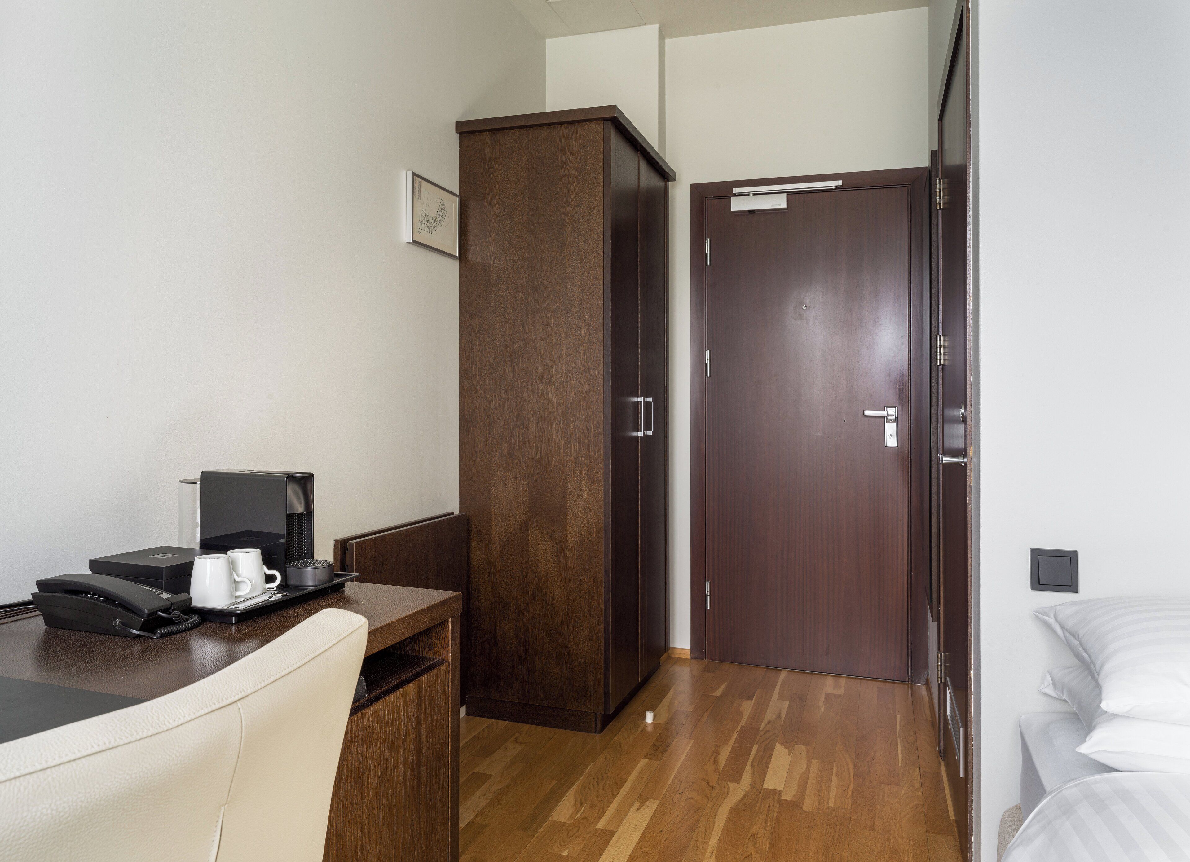 A hotel room with a desk, a telephone, a coffee maker, a wardrobe, and a bed.