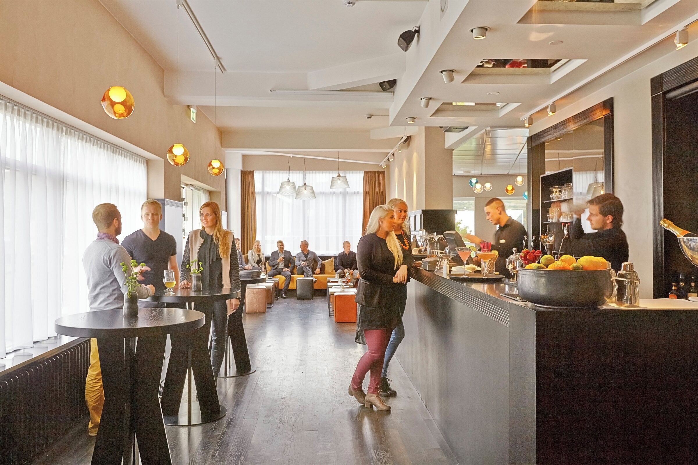 Un espace bar moderne avec des tables rondes, un barman et un comptoir où sont disposés des fruits et des bouteilles.