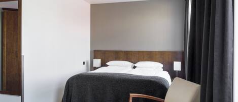 A hotel room with a bed, a chair, a table, and a window with curtains.