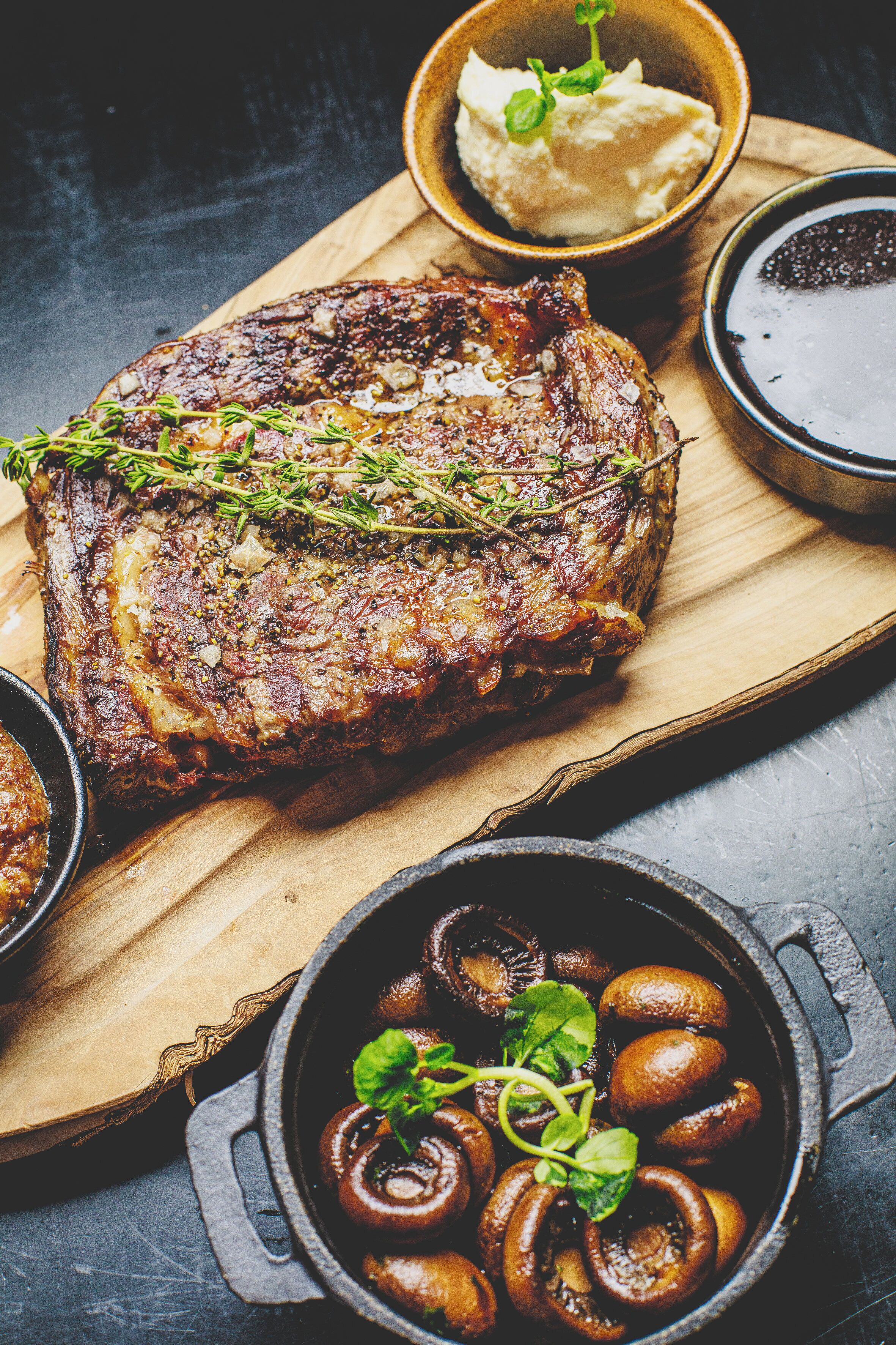 Un steak aux champignons, accompagné d’une portion de purée de pommes de terre, le tout servi sur une planche en bois.