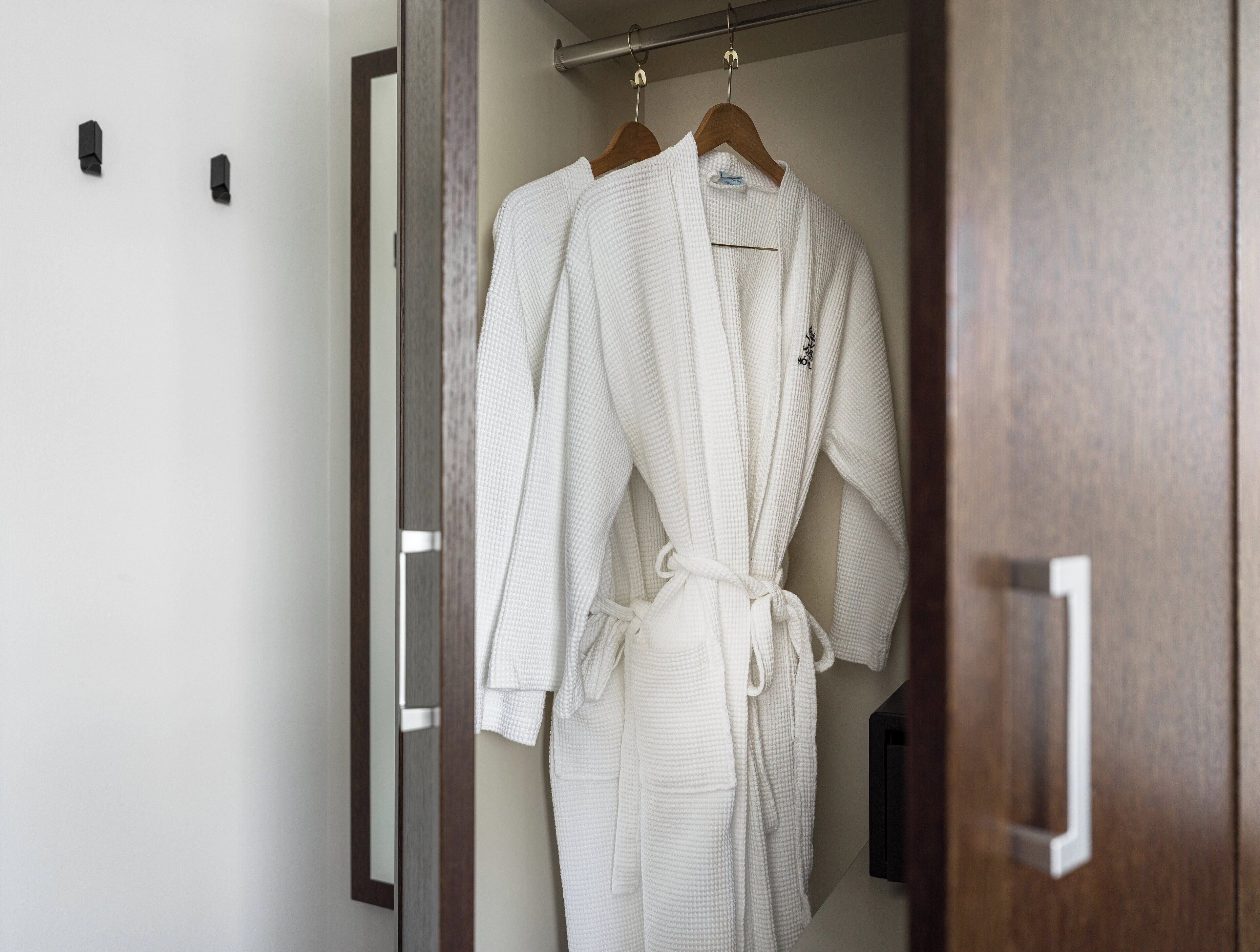 A white robe hanging on a wooden hanger in a closet with a wooden door and a metal handle.
