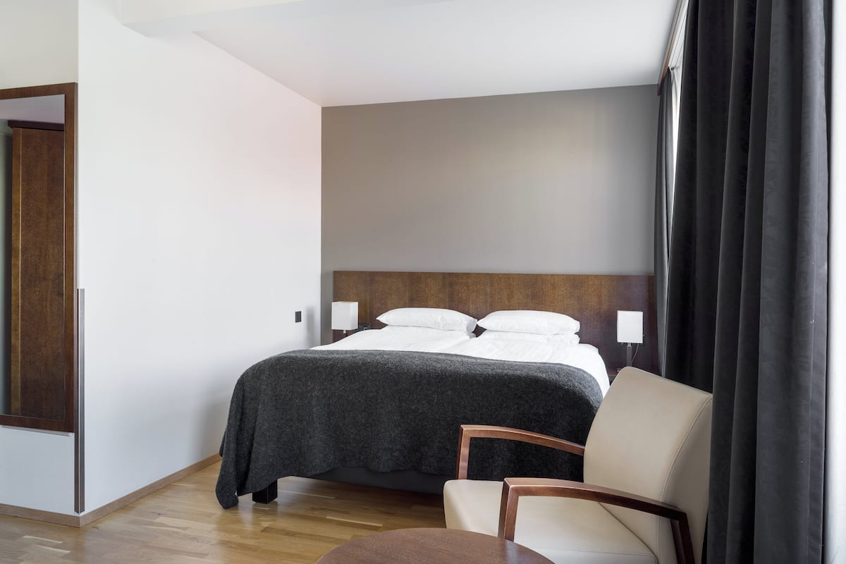 Ein Hotelzimmer mit Bett, Sessel, Tisch und einem Vorhangfenster.