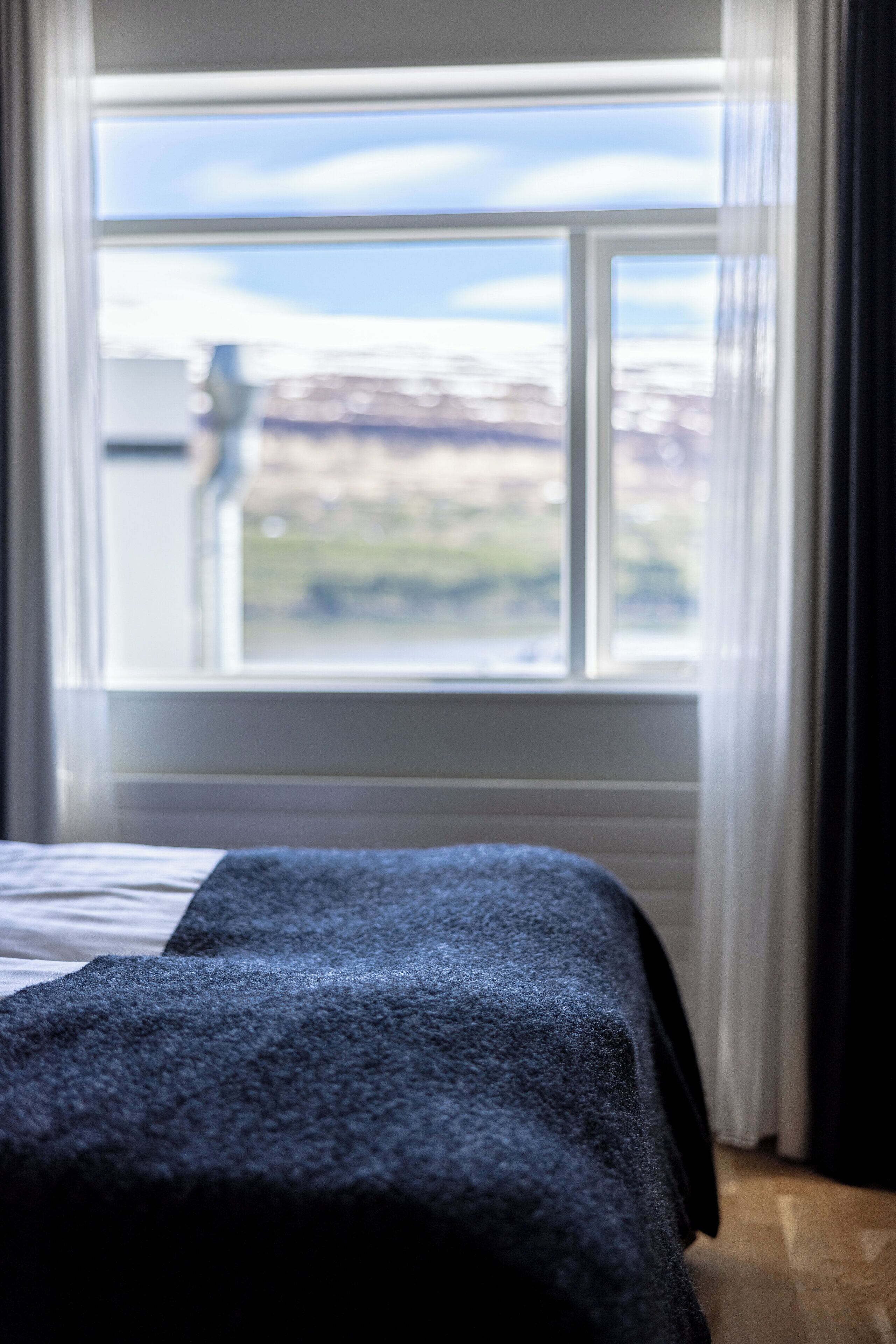 A bed with a dark cover in a room with a large window.