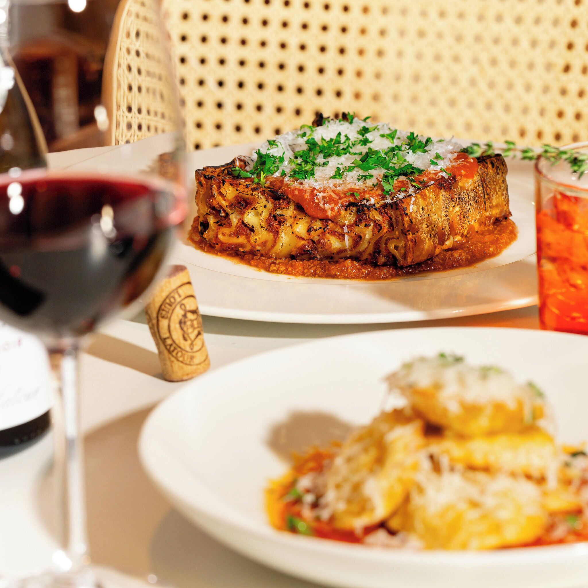 Una mesa de comedor con un plato de comida, una copa de vino tinto y una botella de vino.
