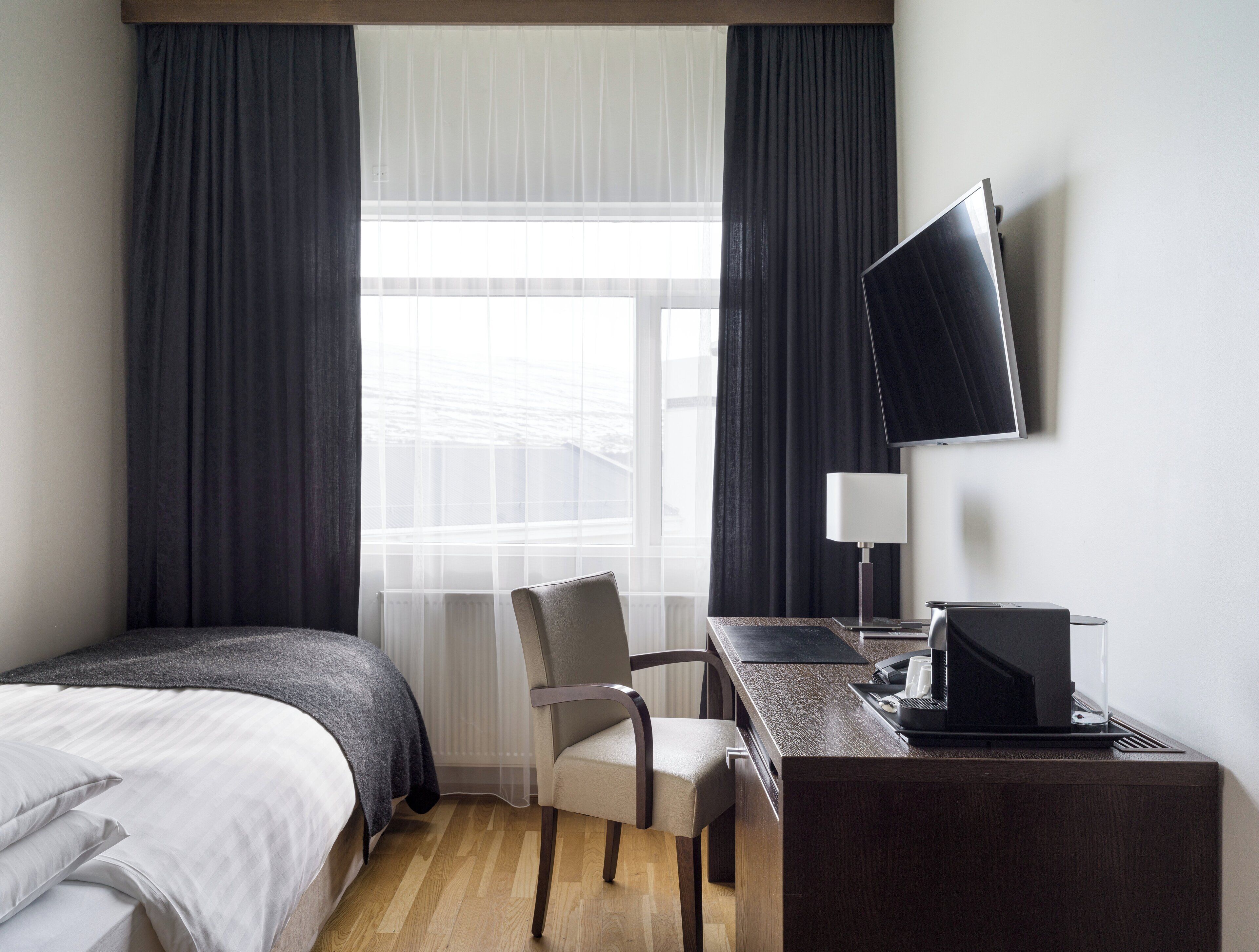 A hotel room with a bed, a desk with a computer, a chair, and a TV on the wall.