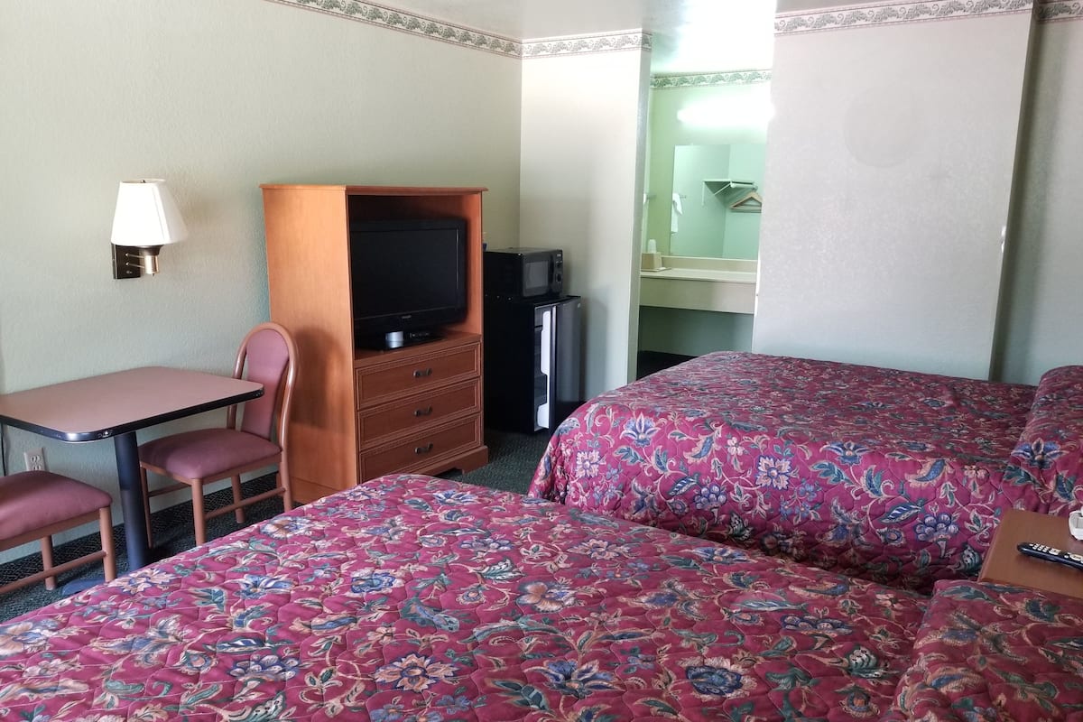 A hotel room with two beds, a desk with a chair, a television, and a small kitchenette.