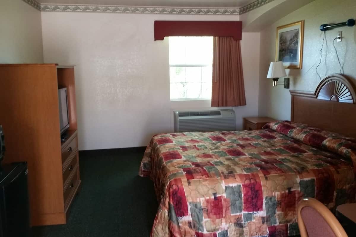A hotel room with a bed, a desk, a television, a heater, and a window with curtains.