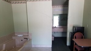 A bathroom with a bathtub, a sink, and a mirror. There is a table and chairs in the adjacent room. - Haltom Inn (Haltom City)