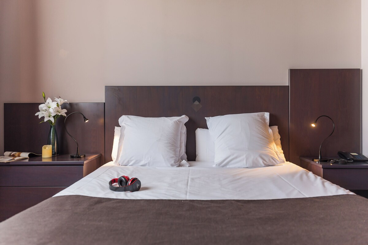 A neatly made bed with white bedding, a bedside table with a lamp, and a vase with flowers.