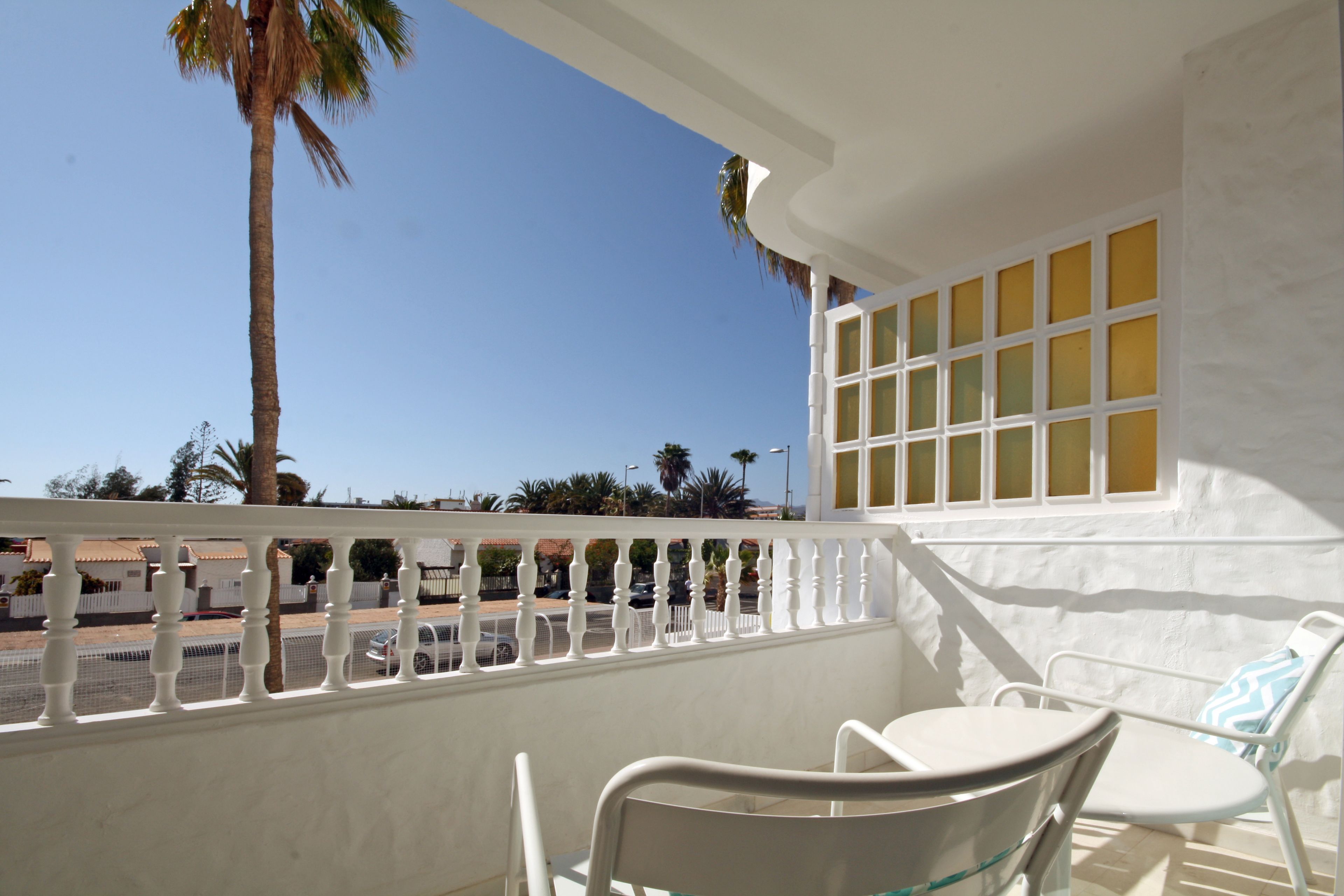 A balcony with white railings, a white chair, a table, and a window with yellow-tinted glass.
