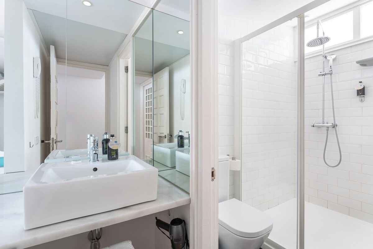 A modern bathroom with a large white sink, a glass shower enclosure, and a toilet.