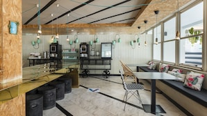 A modern bar area with a long counter, seating with cushions, and pendant lighting.