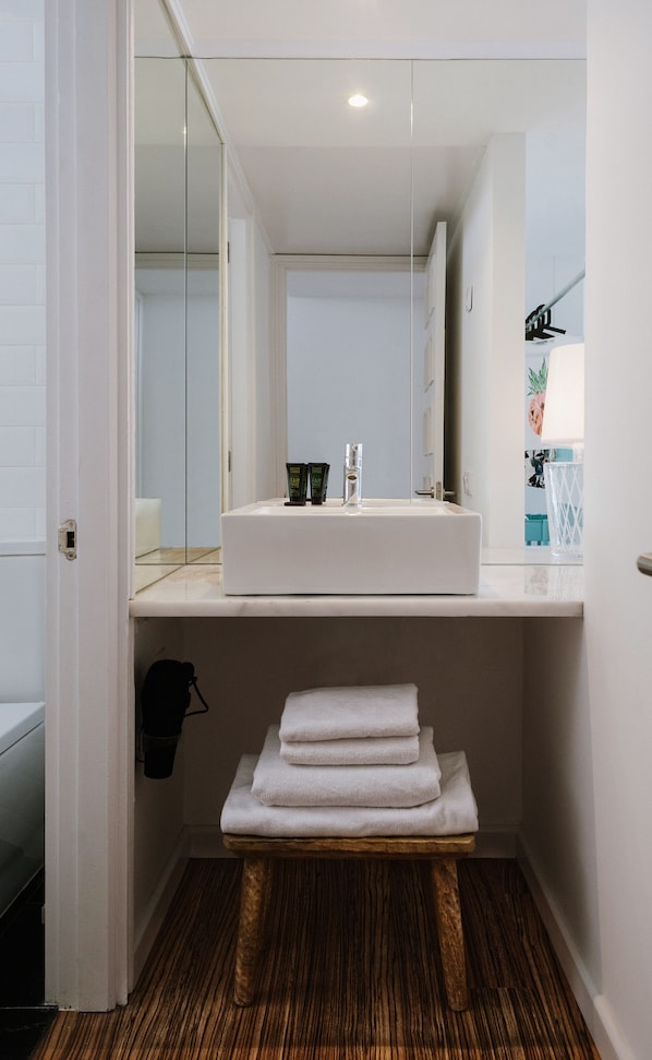 Un baño con un lavabo blanco, un espejo y un banco de madera con toallas.