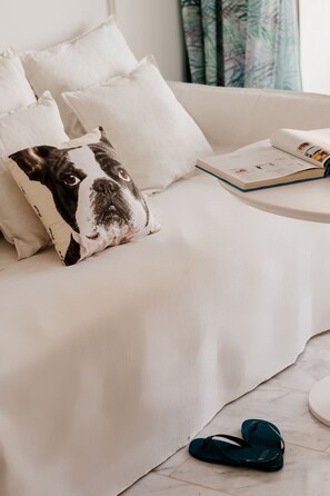 A white sofa with a pillow featuring a dog, a book, and a pair of flip-flops on the floor.