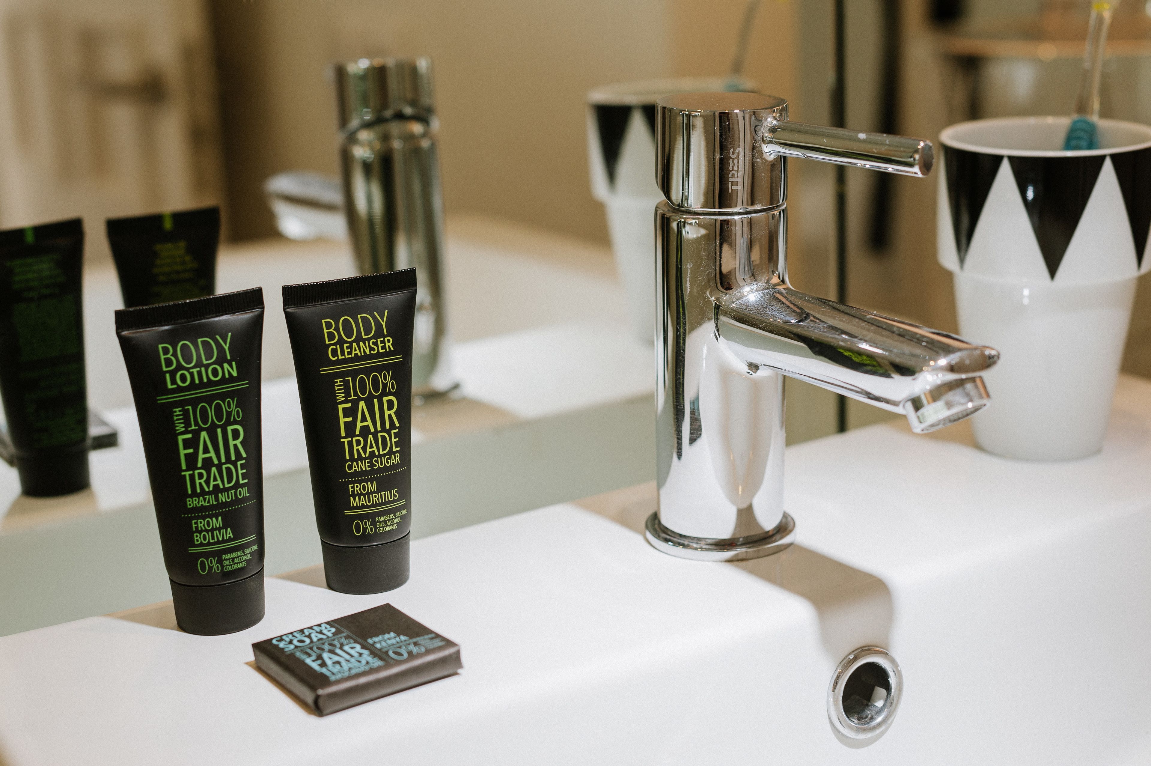 A bathroom with a modern faucet, a mirror, and toiletries including body lotion and body cleanser.