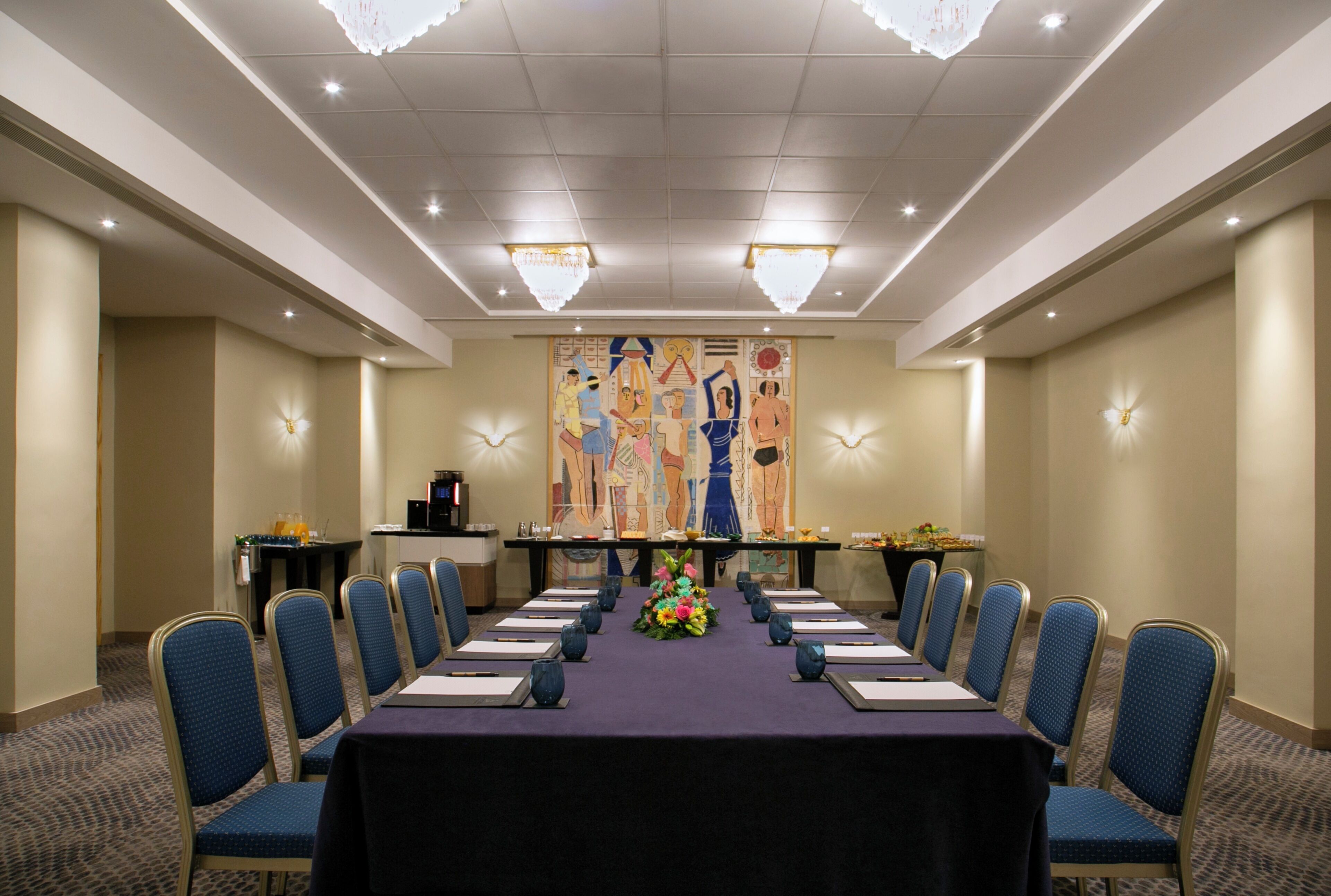 A conference room with a long table, blue chairs, and a decorative wall mural.