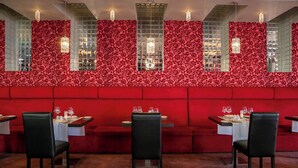 Interior de restaurante con papel tapiz floral rojo, un banco acolchado rojo y mesas dispuestas para comer.