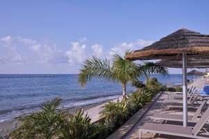 Un resort frente a la playa con una estructura de techo de paja, sillas de descanso y vista al mar.