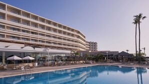 Un hotel con una piscina grande, varios balcones y zonas de estar al aire libre.