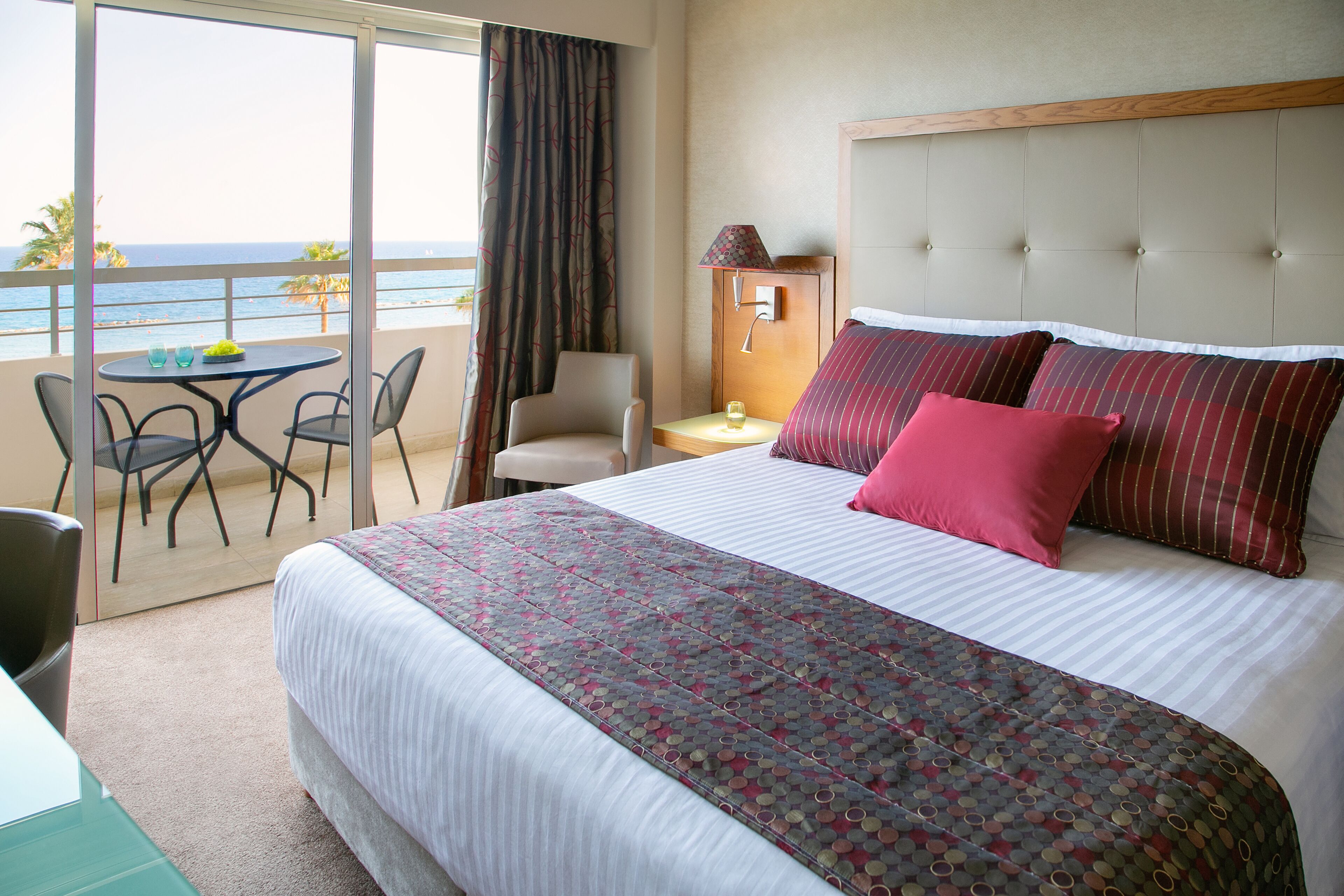 A hotel room with a bed, a desk, a chair, a table, and a view of the ocean.