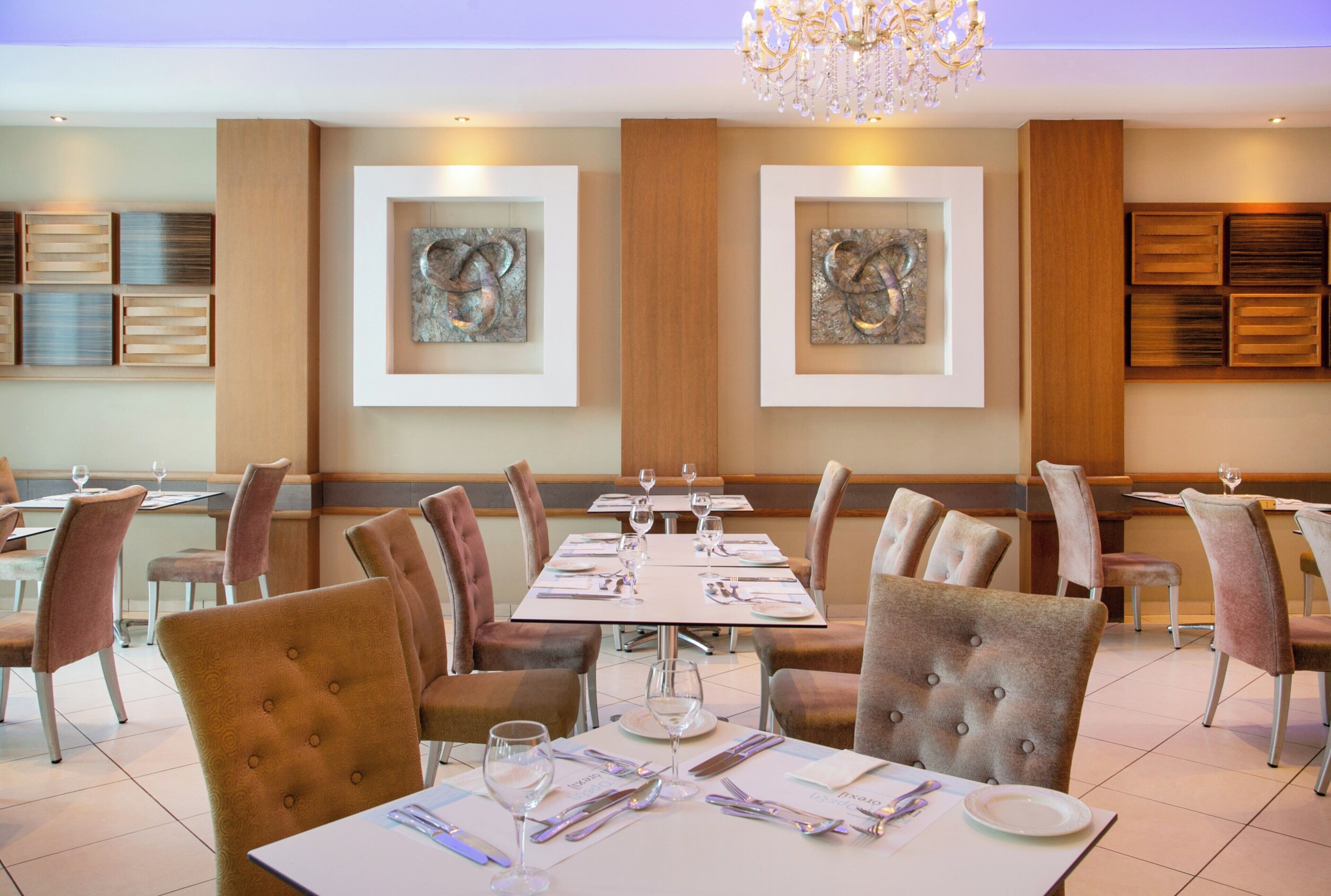A restaurant with tables set for dining, chairs, and artwork on the walls.