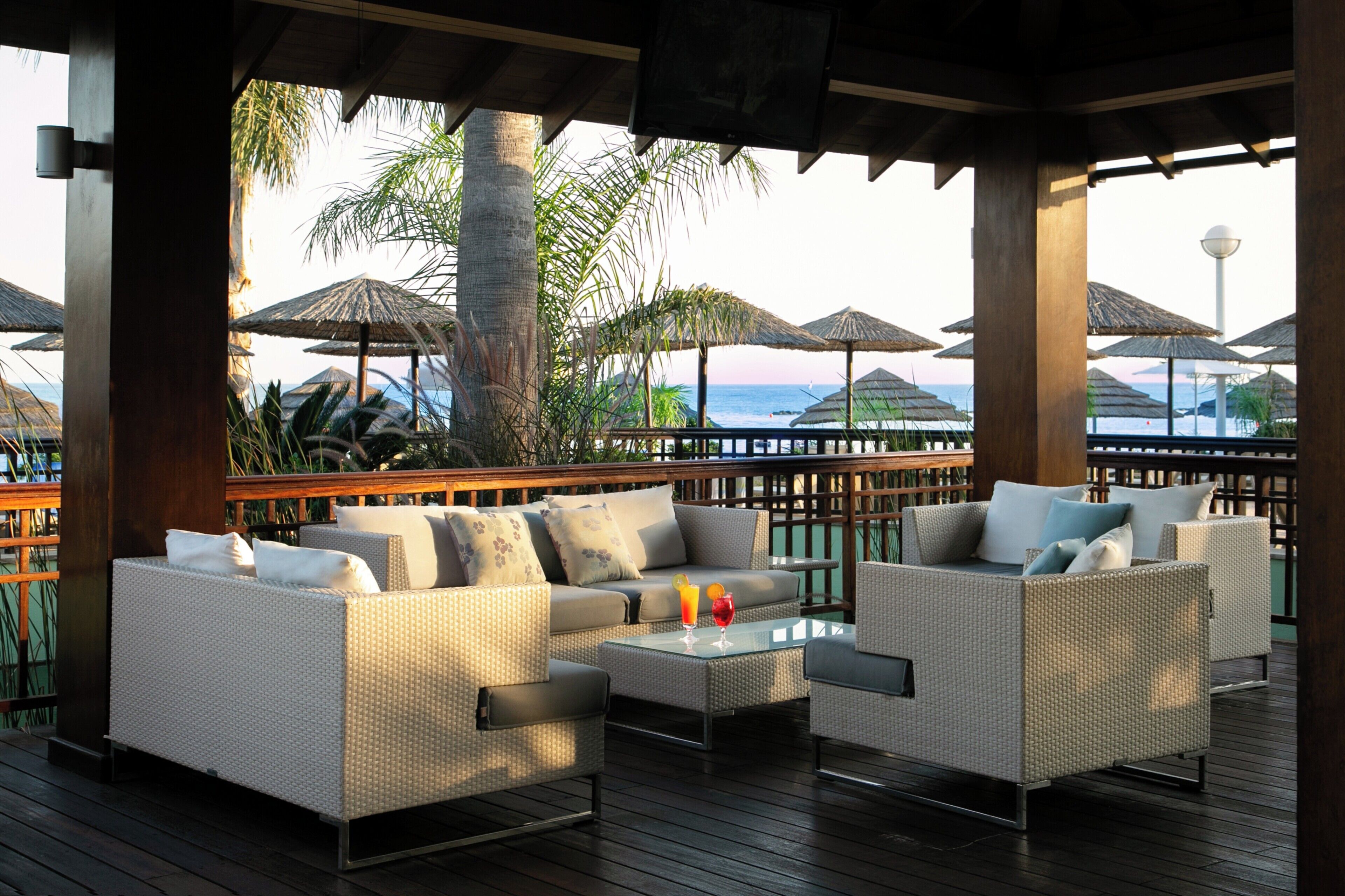 A covered outdoor seating area with wicker furniture and umbrellas, overlooking a beach.