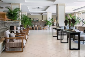 A spacious lobby with a seating area featuring wooden chairs and sofas, a coffee table, and decorative plants.