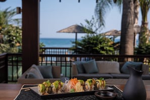 Una mesa con sushi, un jarrón negro y vista al océano.